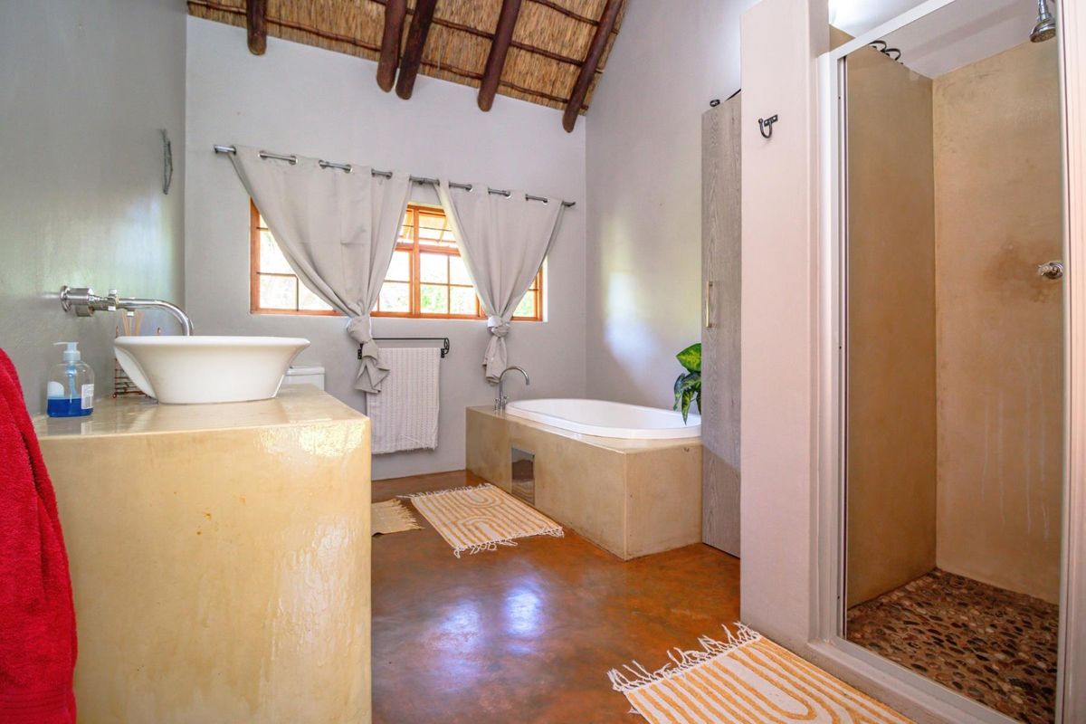 A rustic-style bathroom featuring a built-in vanity with a vessel sink, a sunken bathtub, a separate shower, and a high thatched ceiling.