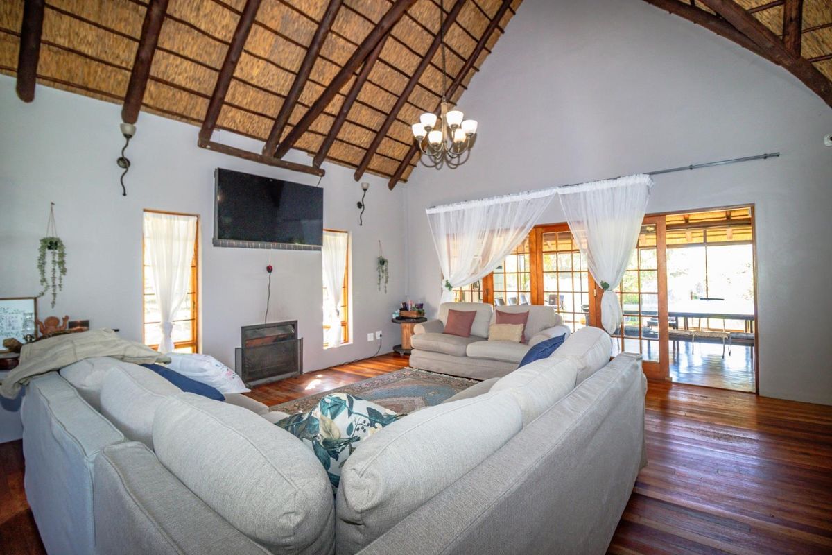 Spacious living room featuring a high vaulted thatched ceiling, exposed timber beams, hardwood flooring, and direct access to an outdoor patio area.