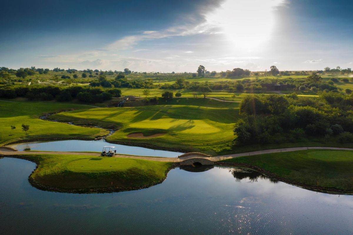 Aerial view of a scenic golf course landscape featuring manicured greens, water hazards, and a stone bridge.