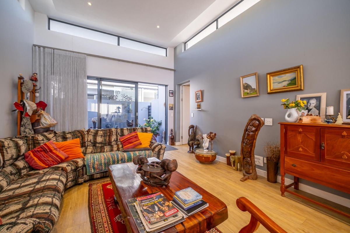 Spacious living room featuring high ceilings with clerestory windows, light wood-look flooring, and large sliding glass doors providing access to the outdoor patio area.