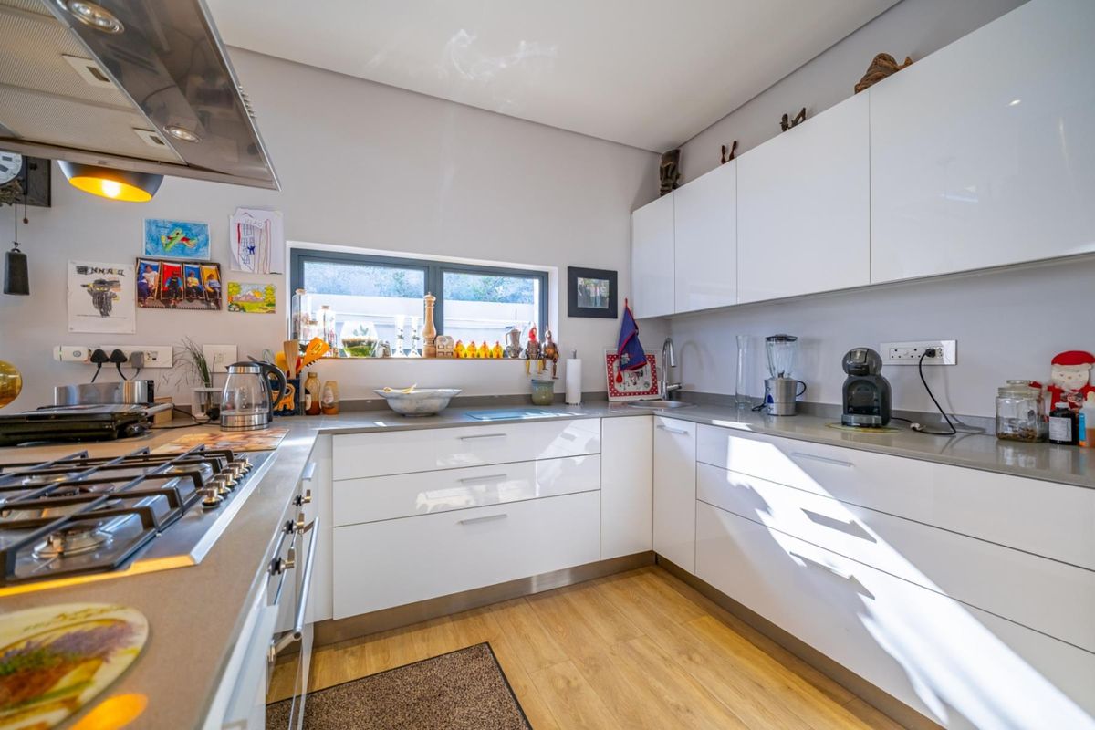 Modern kitchen featuring white high-gloss cabinetry, stone countertops, a built-in gas hob, and an integrated extractor fan with wood-look flooring.