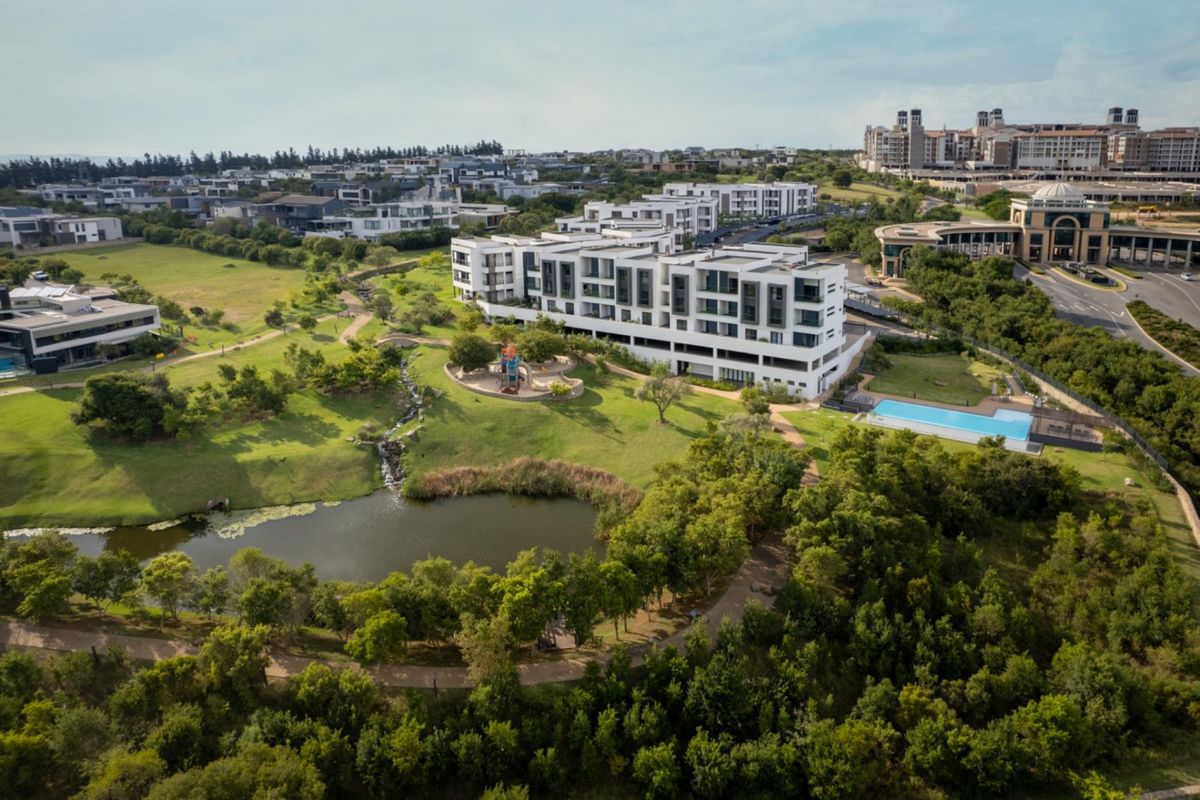 Aerial view of a modern apartment complex set within a landscaped estate featuring a swimming pool, pond, and walking paths.