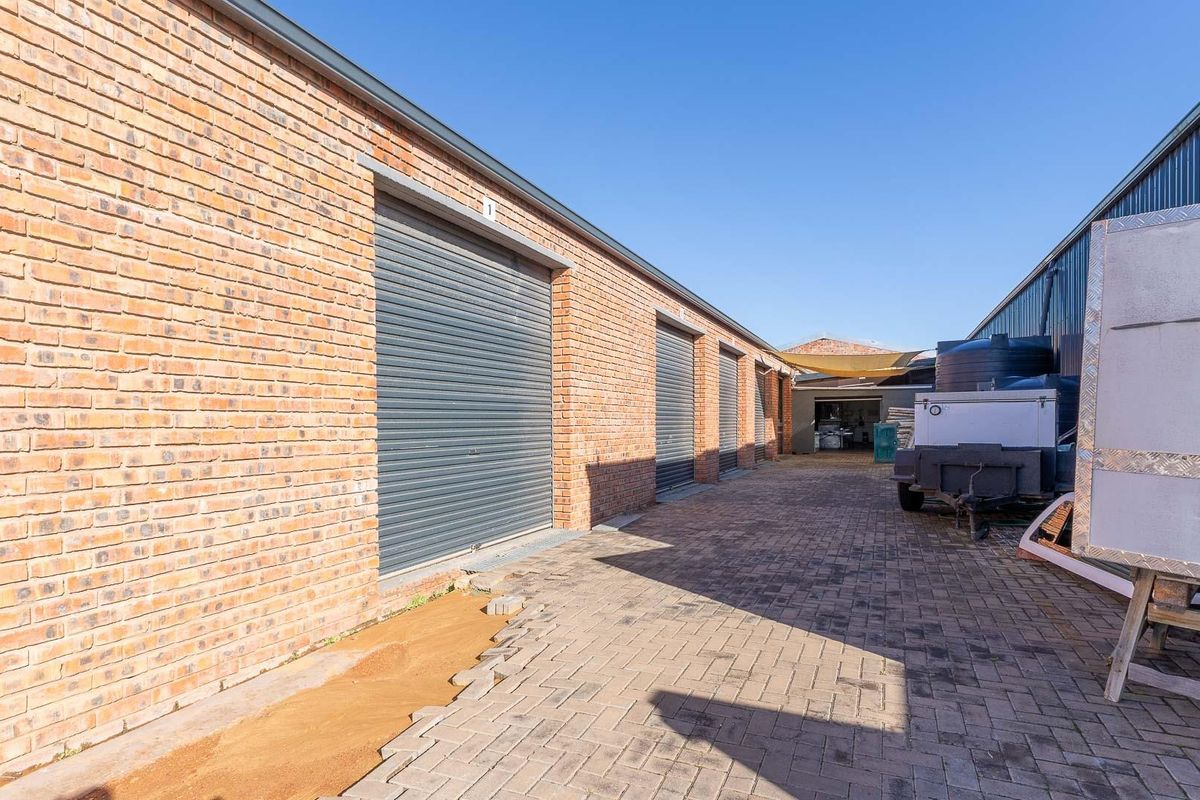 Exterior view of a commercial storage facility featuring multiple roller shutter doors, brick facade, and paved driveway access.