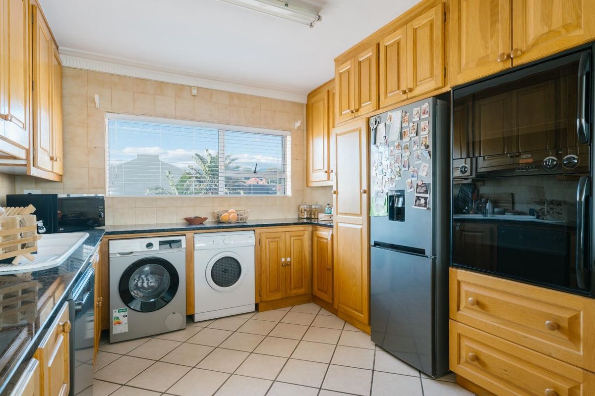 A functional kitchen featuring timber cabinetry, dark granite countertops, tiled splashbacks, and integrated appliance spaces for laundry and cooking.