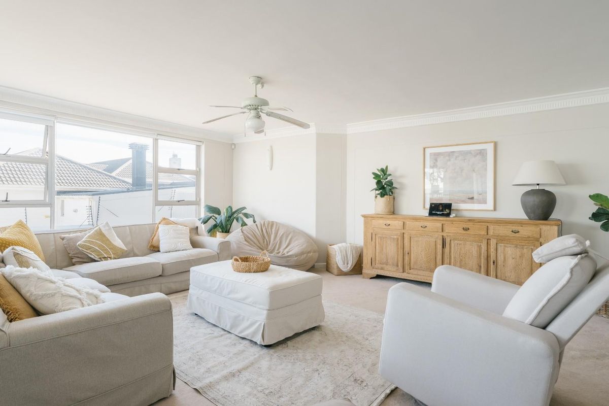 Bright and spacious living room featuring large windows, neutral carpeting, and a ceiling fan, creating a comfortable and inviting atmosphere.