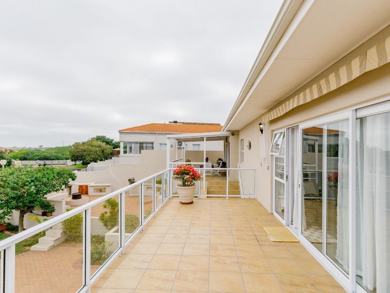 A spacious elevated balcony featuring tiled flooring, a modern glass balustrade, and a retractable awning, providing access to the home via sliding glass doors.