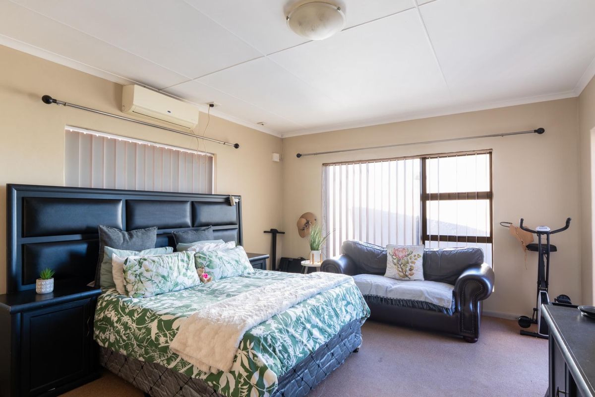 Spacious bedroom featuring a wall-mounted air conditioning unit, large windows with vertical blinds, and neutral wall tones.