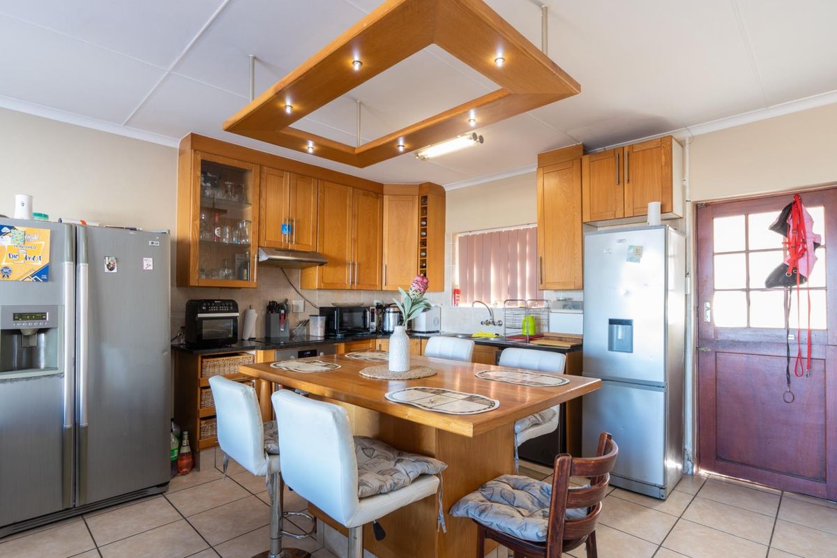 A functional kitchen featuring wooden cabinetry, a central breakfast island with integrated lighting, tiled flooring, and direct access to the exterior.