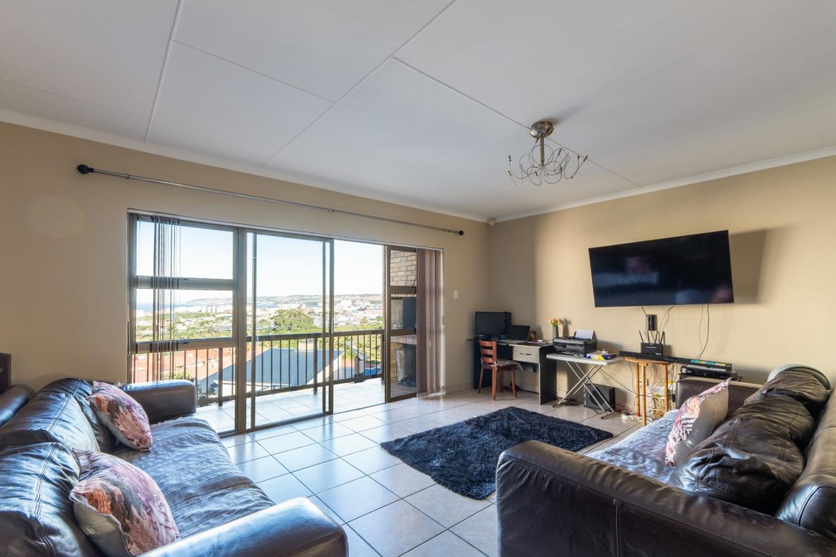 Spacious living area featuring large sliding glass doors that open onto a balcony with expansive coastal and urban views.