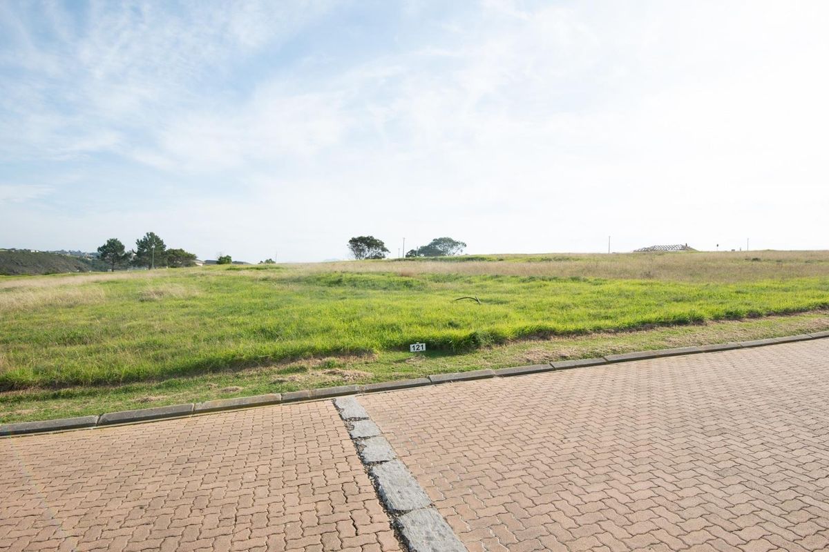 A vacant residential plot of land featuring level grass terrain, accessible from a paved street with established kerbing.