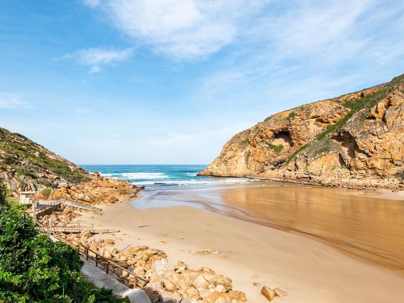 A scenic view of a coastal landscape featuring rocky cliffs, a sandy beach, and an estuary meeting the ocean.