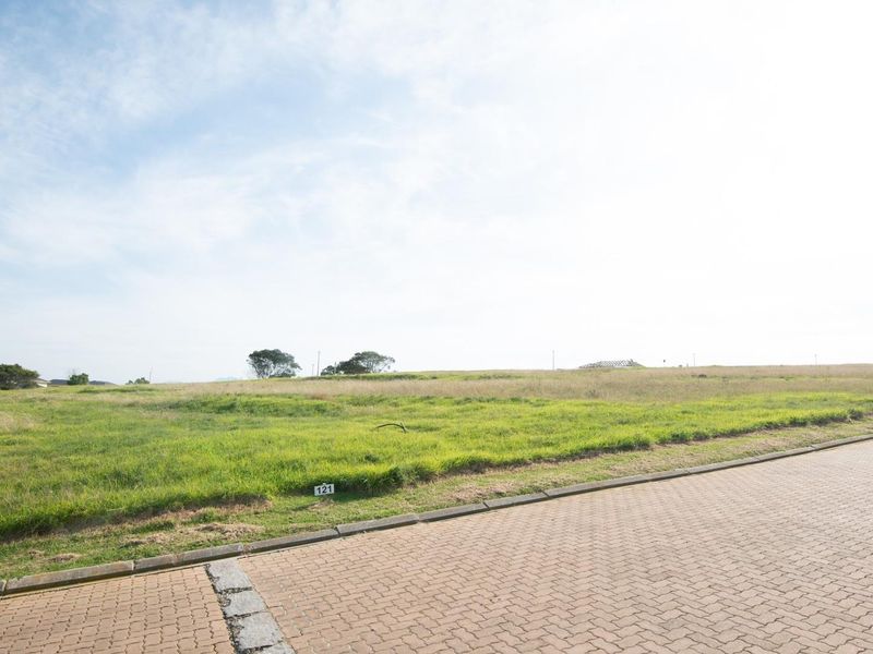 A vacant residential plot featuring a level grassed area with paved street access and established kerbing.