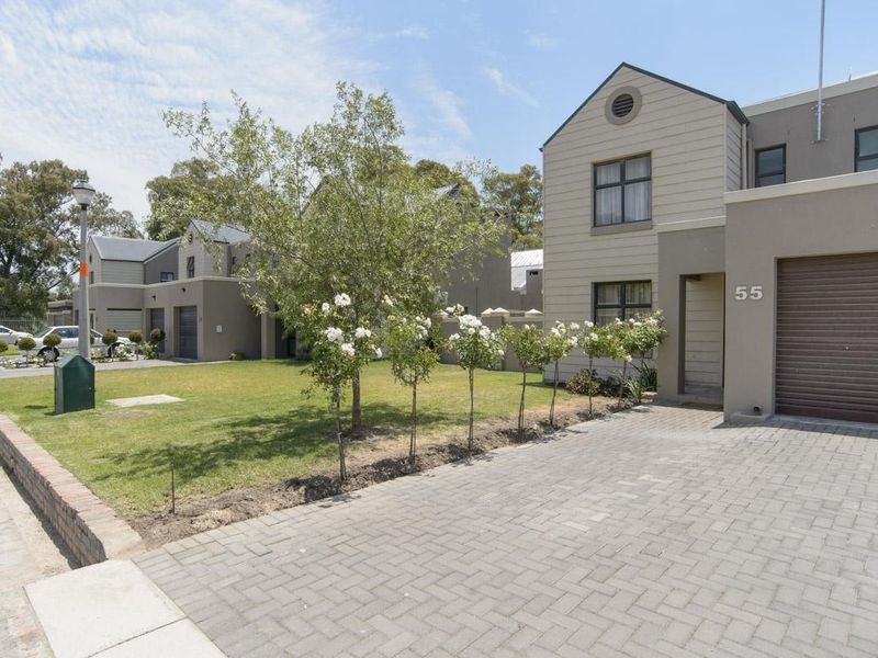 Front elevation of a modern two-story townhouse featuring a paved driveway, single garage, and a well-maintained front garden with established trees.