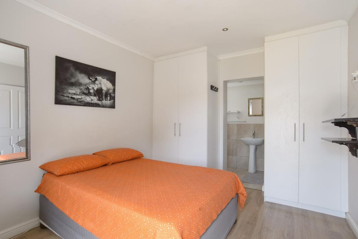 A well-maintained bedroom featuring built-in cupboards, laminate flooring, and an en-suite area with a pedestal basin.