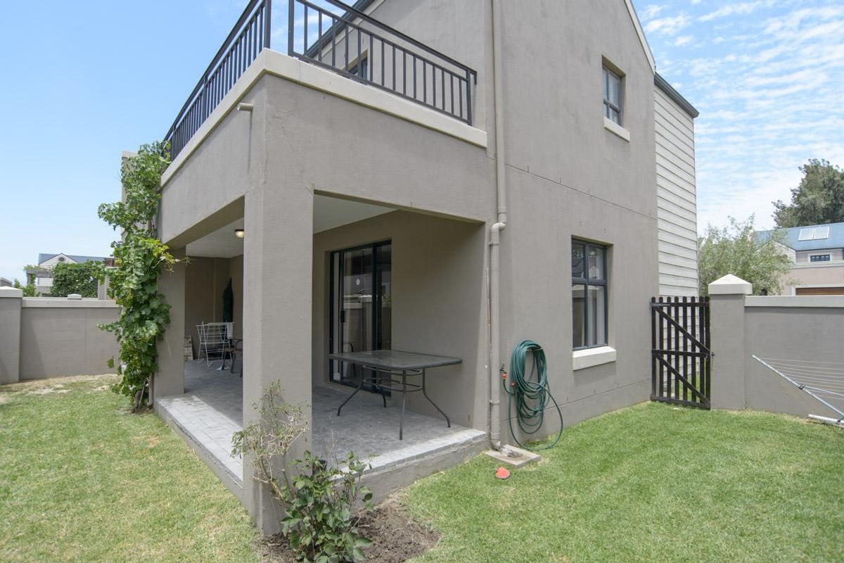 Rear view of the property featuring a covered patio, an upper-level balcony with metal railings, and a private garden area with boundary walls.