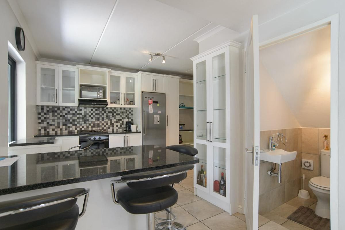 Modern kitchen featuring granite countertops, mosaic backsplash, built-in appliances, and an adjacent guest toilet with tiled finishes.