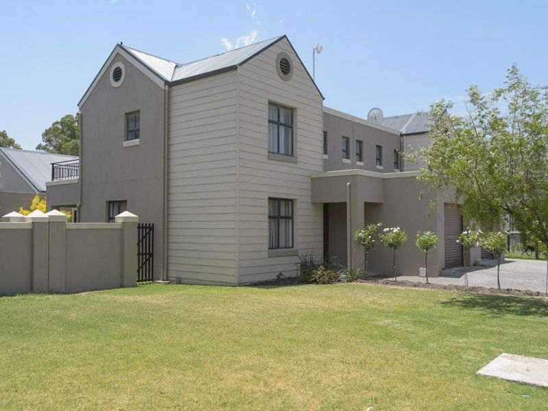 A well-maintained double-story residential property featuring a neutral facade, metal roofing, a paved driveway, and a private front garden with boundary walling.