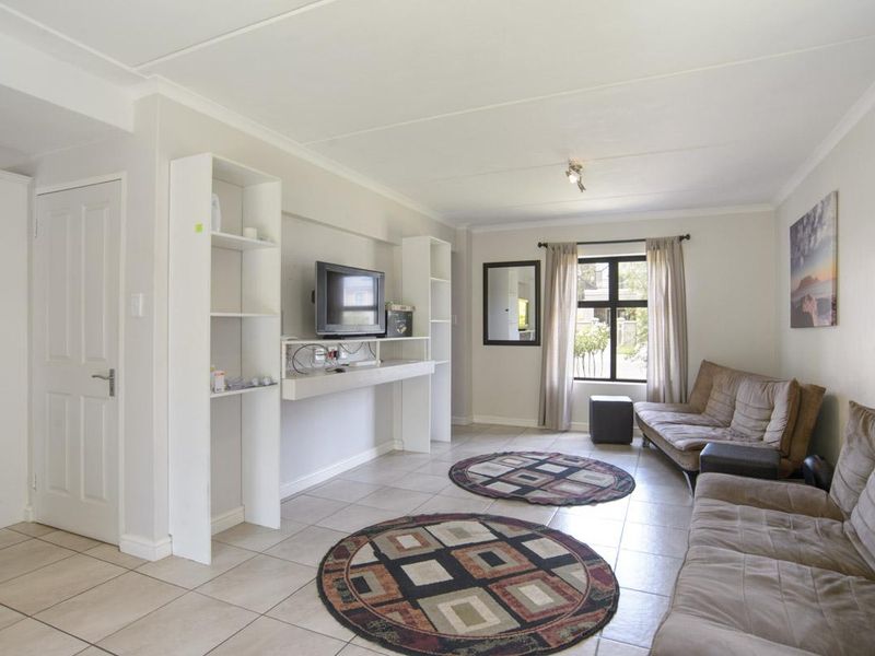 A bright living room featuring neutral tiled flooring, coved ceilings, and built-in shelving units, offering a functional and well-lit space.