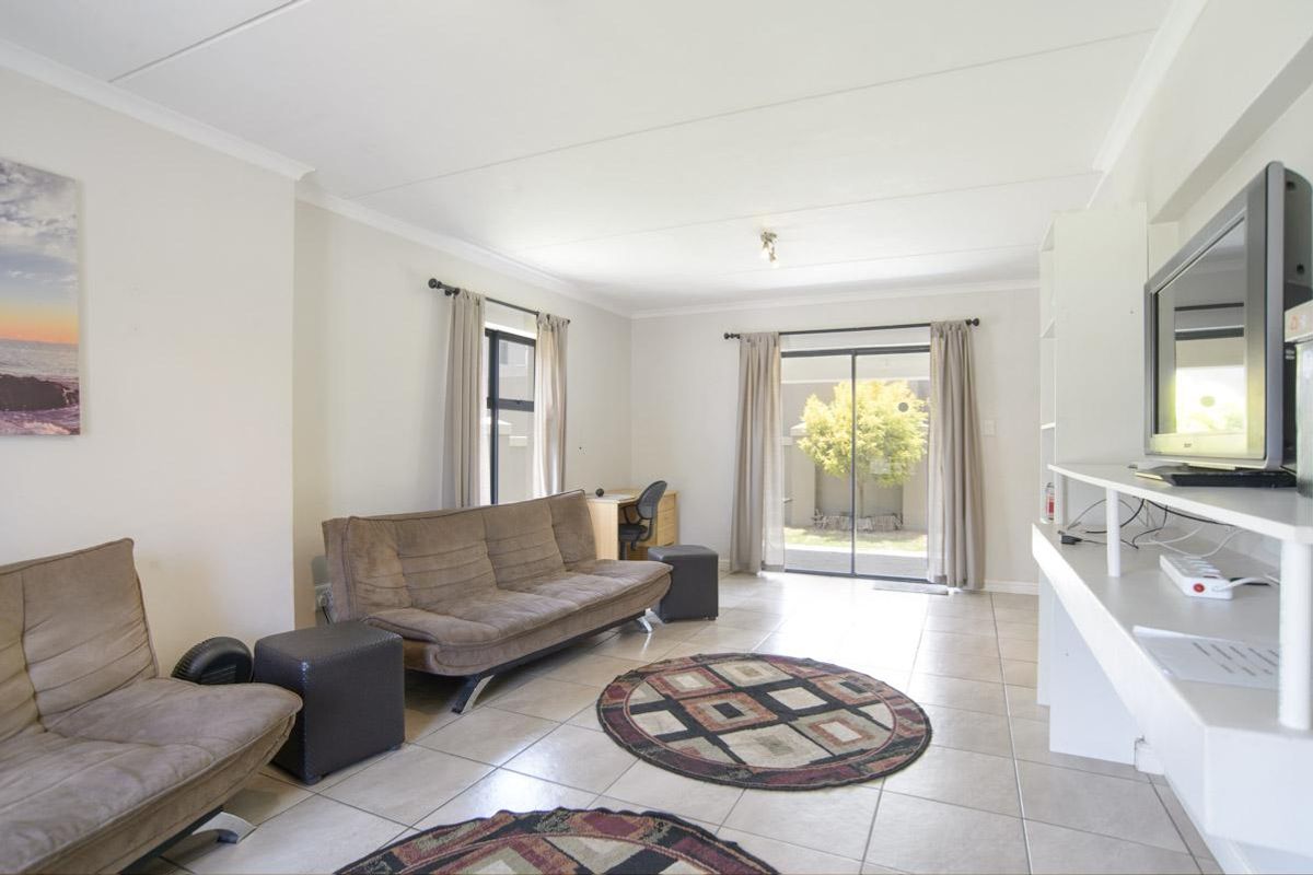 A bright living room featuring neutral tiled flooring, built-in shelving, and sliding glass doors providing access to the rear garden area.