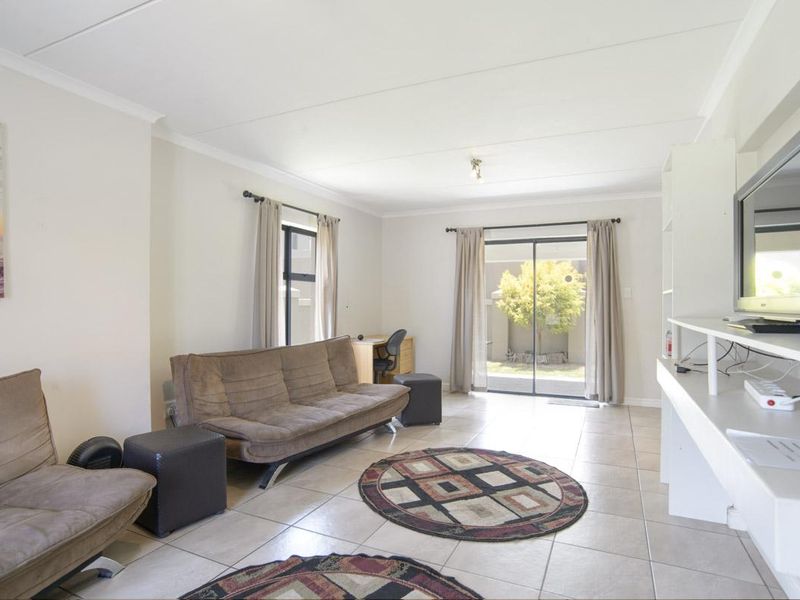 A bright living room featuring neutral tiled flooring, built-in shelving, and sliding glass doors providing access to the rear garden area.