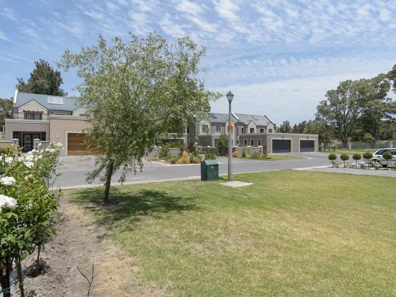 A view of the residential street featuring well-maintained lawns, paved driveways, and modern garage facades within a quiet estate setting.