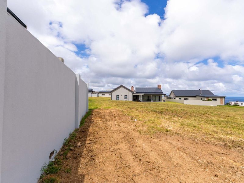A view of a vacant residential plot featuring a boundary wall and open land with surrounding coastal neighborhood homes.