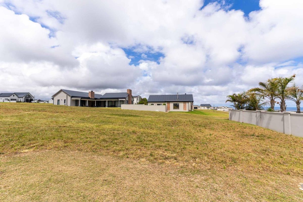 A wide-angle view of the rear exterior of a modern residential property featuring a large lawn, boundary wall, and covered patio area.