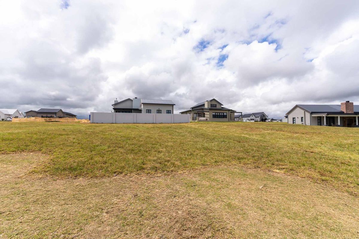 A view of a vacant residential plot in a developed estate, showcasing the surrounding modern homes and open grassed land.