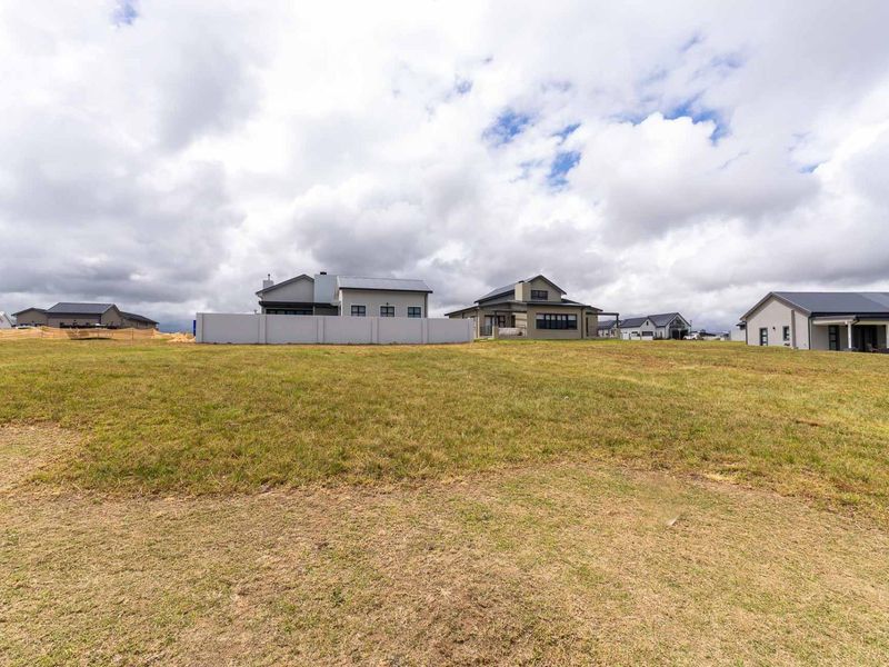 A view of a vacant residential plot in a developed estate, showcasing the surrounding modern homes and open grassed land.