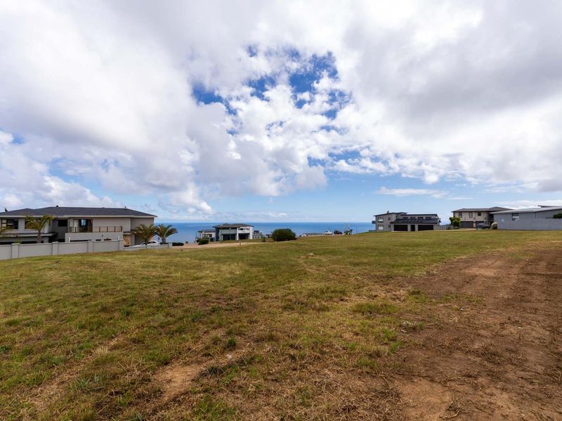 A vacant residential plot of land featuring open grass areas and boundary walls, situated in a coastal neighborhood with ocean views.