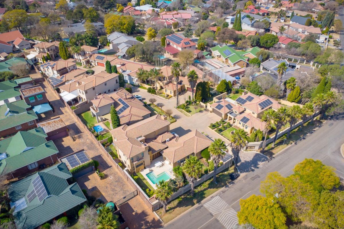 An aerial view of a residential estate featuring multiple houses with tiled roofs, private swimming pools, and established landscaping.