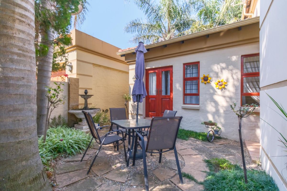 A charming rear courtyard featuring stone paving, a decorative fountain, and direct access to the home through classic red-framed double doors.