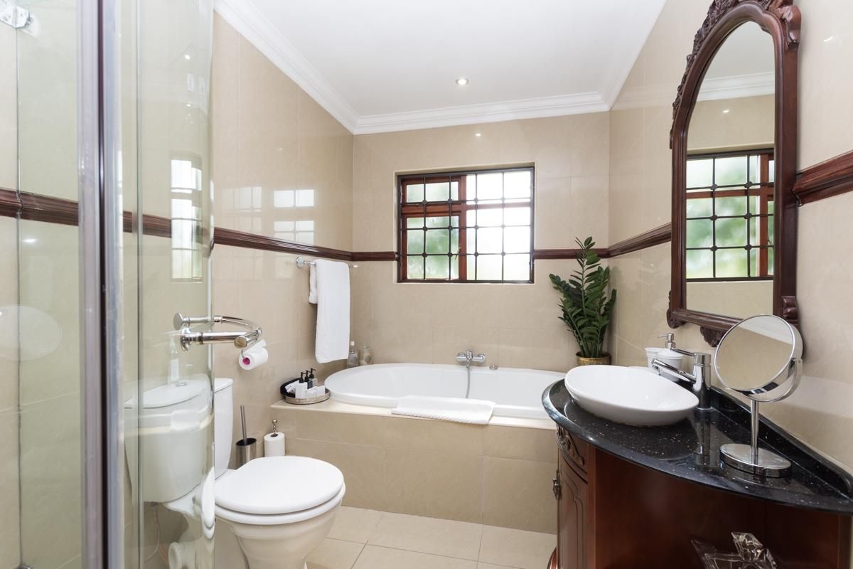 A well-maintained hotel bathroom featuring a built-in bathtub, a glass-enclosed shower, a vanity with a vessel sink, and neutral wall tiling.