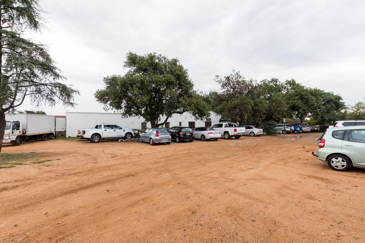 An unpaved, open-air dirt parking area serving the commercial property, featuring mature trees and direct access to the building facade.