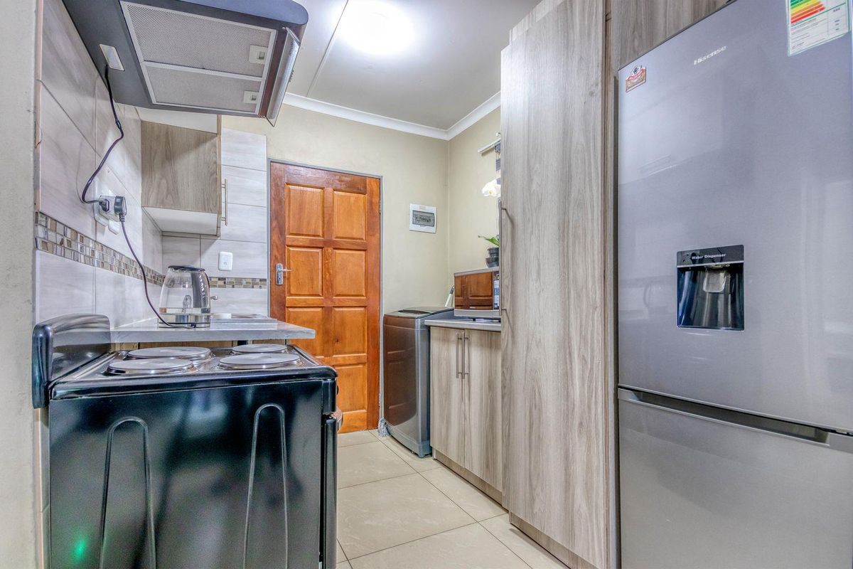 A functional kitchen featuring wood-look cabinetry, tiled backsplash, and tiled flooring, providing a practical workspace with integrated storage and essential fixtures.