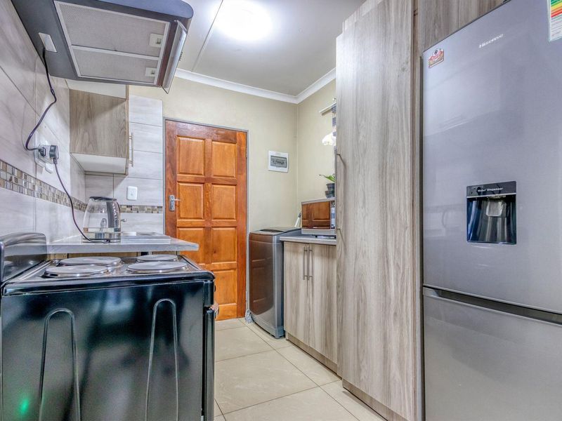 A functional kitchen featuring wood-look cabinetry, tiled backsplash, and tiled flooring, providing a practical workspace with integrated storage and essential fixtures.