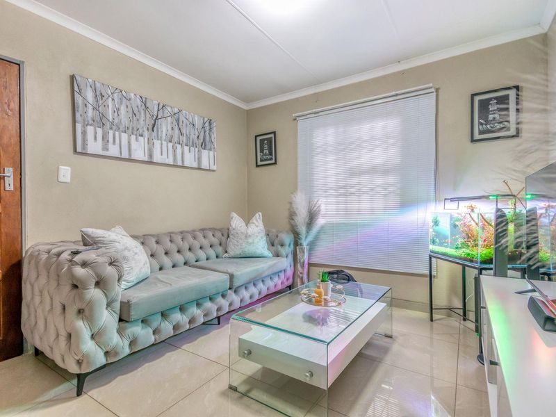 A well-maintained living room featuring neutral wall tones, tiled flooring, and venetian blinds, providing a comfortable and functional space.