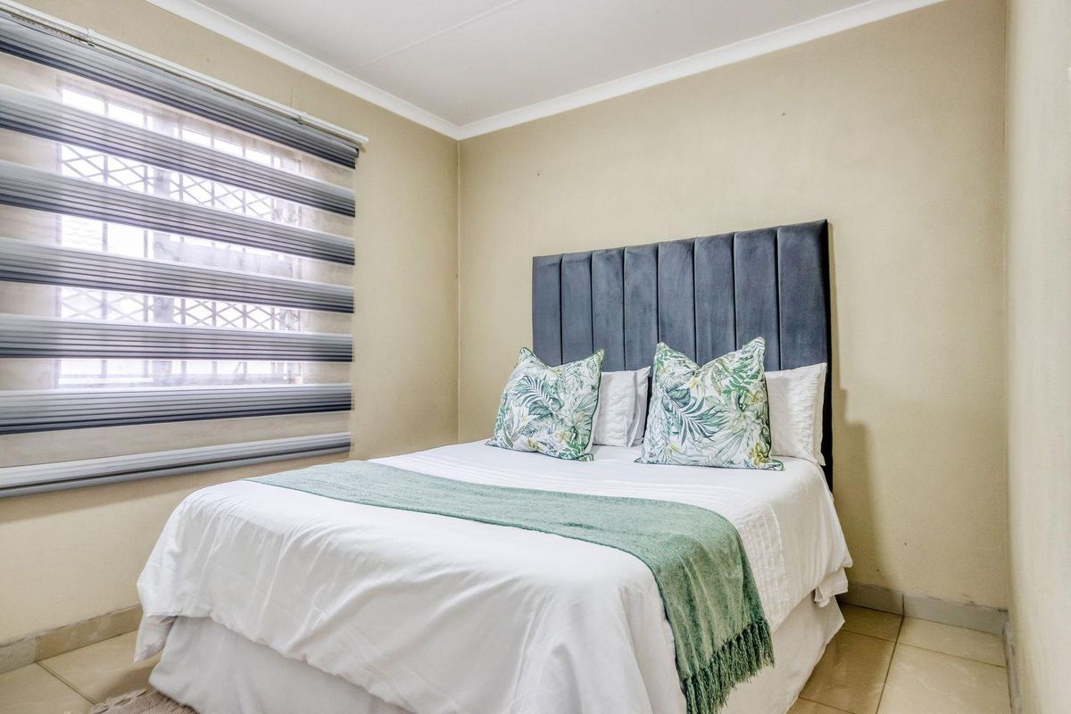 A well-maintained bedroom featuring tiled flooring, security bars on the window, and neutral wall finishes.