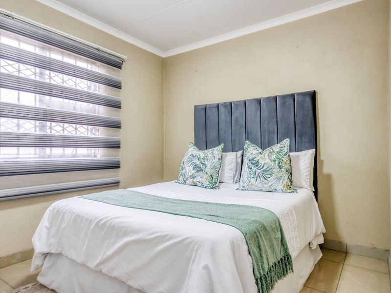 A well-maintained bedroom featuring tiled flooring, security bars on the window, and neutral wall finishes.