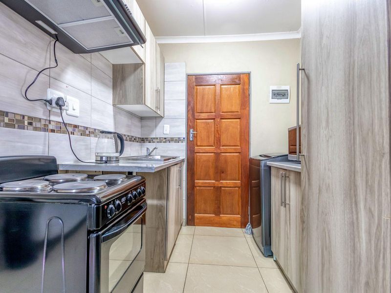 A functional kitchen featuring wood-look cabinetry, tiled backsplash, built-in electric stove with extractor fan, and tiled flooring.