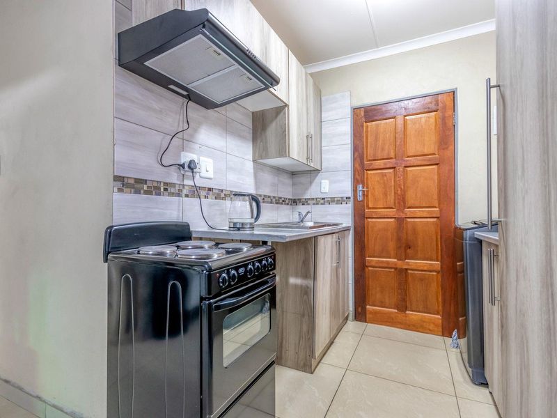 Compact kitchen featuring wood-look cabinetry, tiled backsplash, extractor fan, and tiled flooring, providing a functional workspace with direct access to an exterior door.