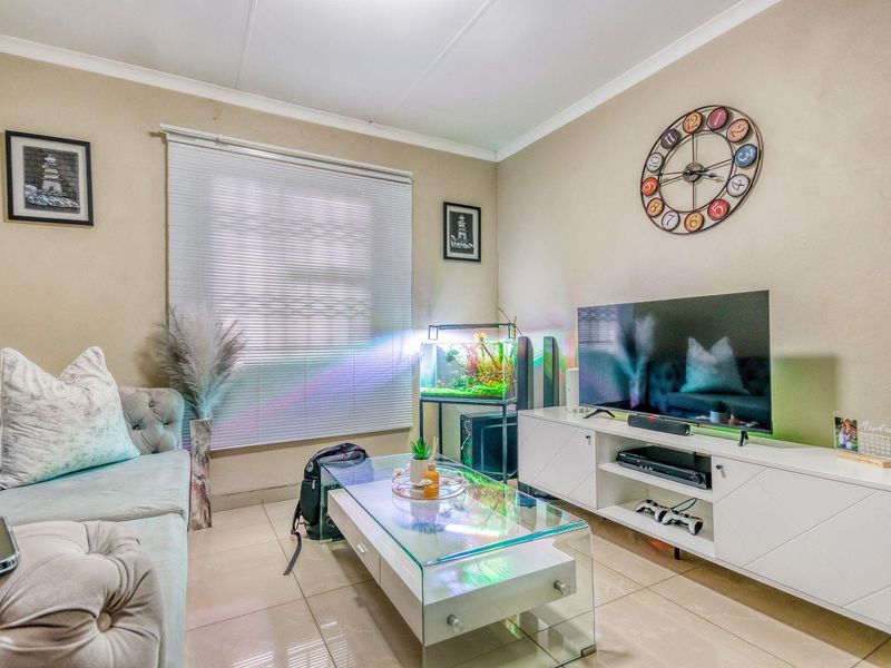 A comfortable living room featuring neutral tiled flooring, coved ceilings, and venetian blinds, providing a functional and well-lit space for relaxation.