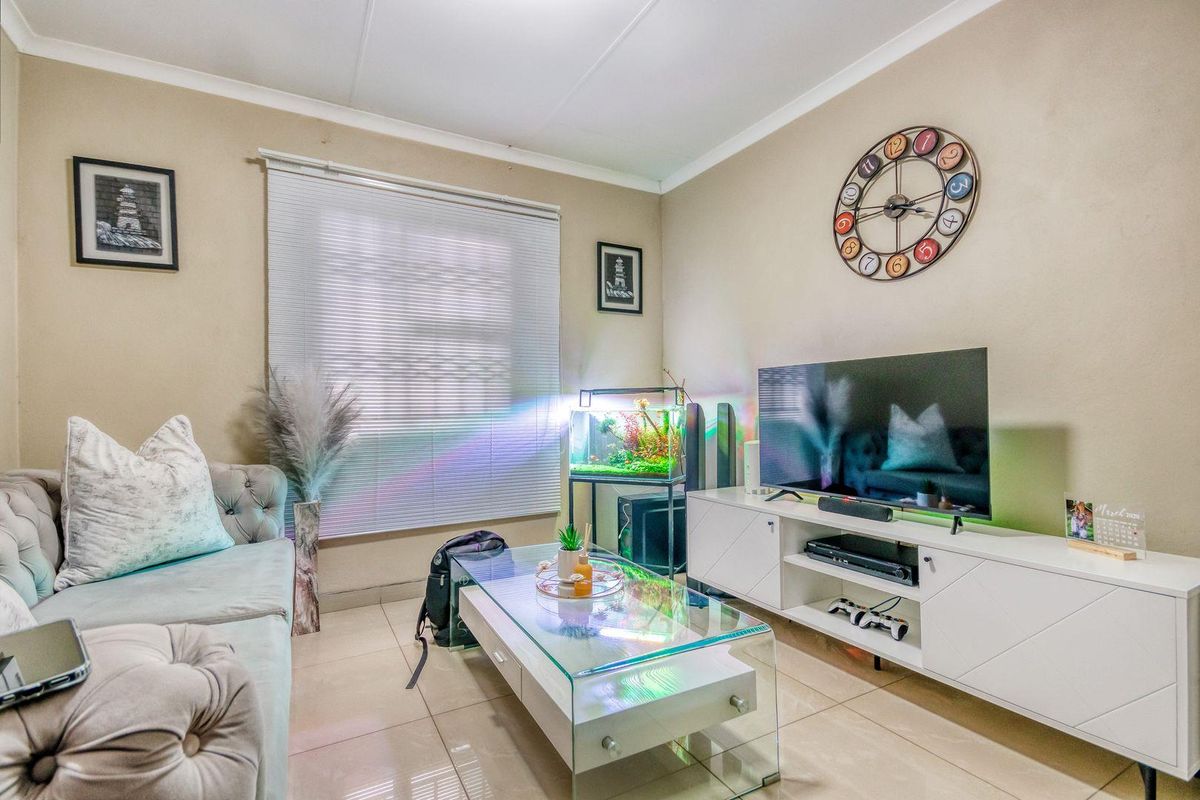 A comfortable living room featuring neutral tiled flooring, coved ceilings, and venetian blinds, providing a functional and well-lit space for relaxation.