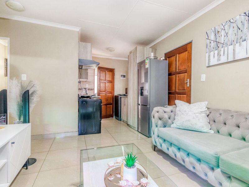 Open-plan living area featuring tiled flooring, neutral walls, and a compact kitchen space with built-in cabinetry and an extractor fan.