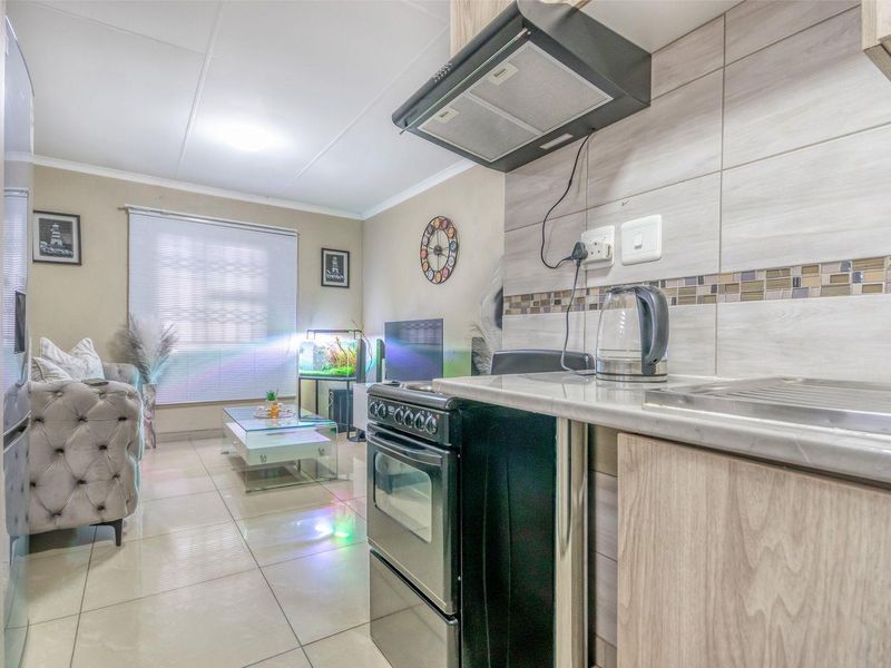 An open-plan living area featuring a compact kitchen with built-in cabinetry, stone countertops, and a tiled backsplash, seamlessly flowing into the adjacent lounge space.
