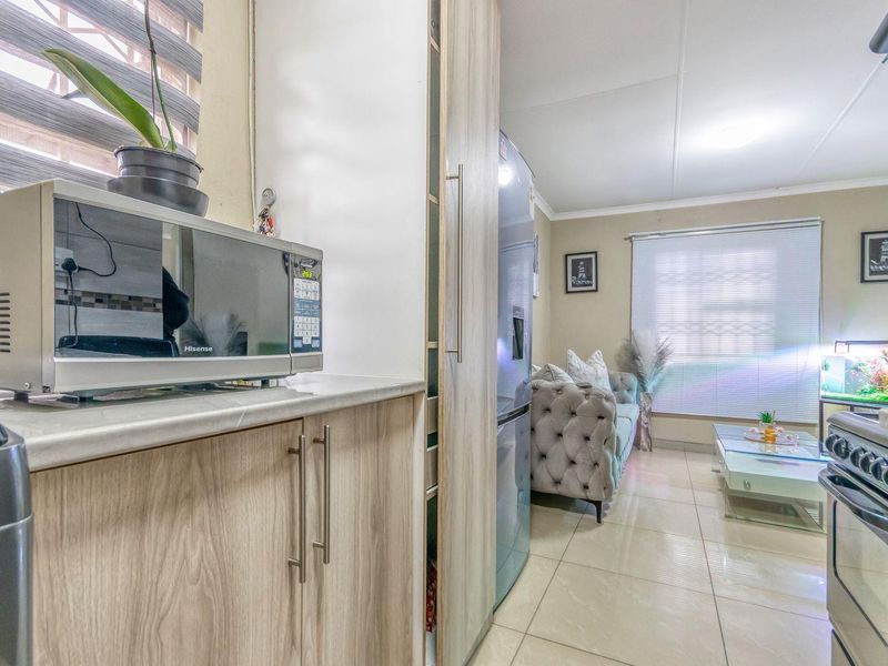 Open plan living area featuring tiled flooring, built-in kitchen cabinetry with laminate countertops, and natural light through venetian blinds.