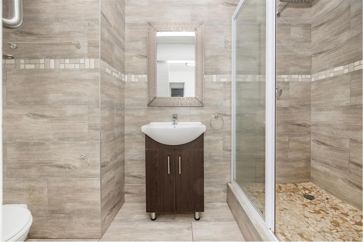 Modern bathroom featuring floor-to-ceiling wood-look tiling, a glass-enclosed shower with pebble-style flooring, a vanity basin, and a wall-mounted mirror.