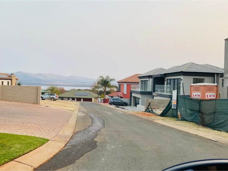 A street view of a residential estate featuring paved roads, surrounding modern homes, and distant mountain and water views.