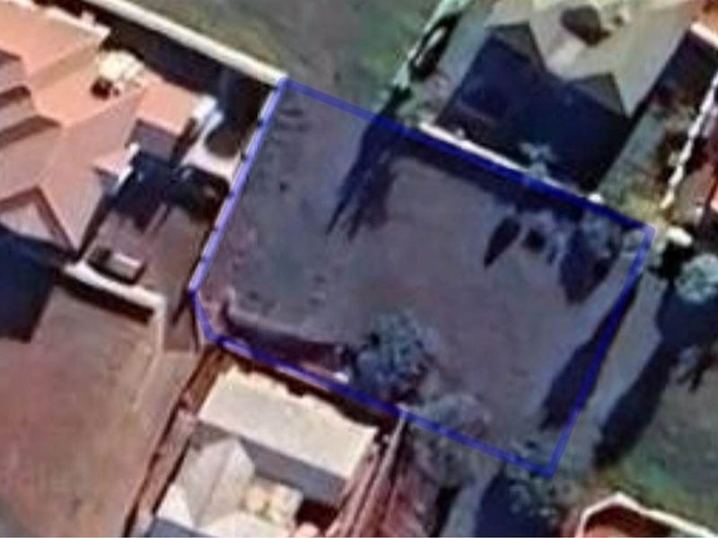 An aerial view of a vacant residential plot outlined in blue, situated within an established neighborhood.