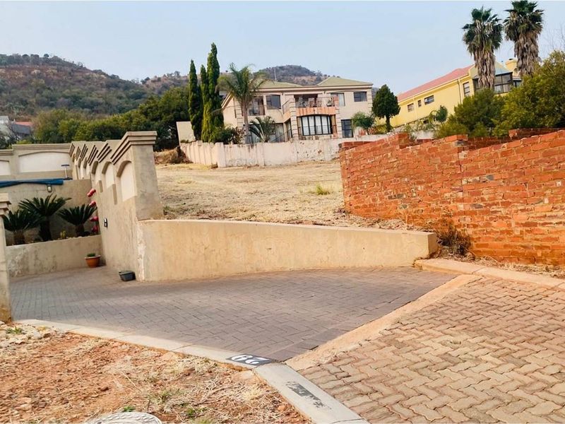 Vacant residential land featuring a paved driveway entrance, established boundary walls, and a gentle slope with surrounding neighborhood views.